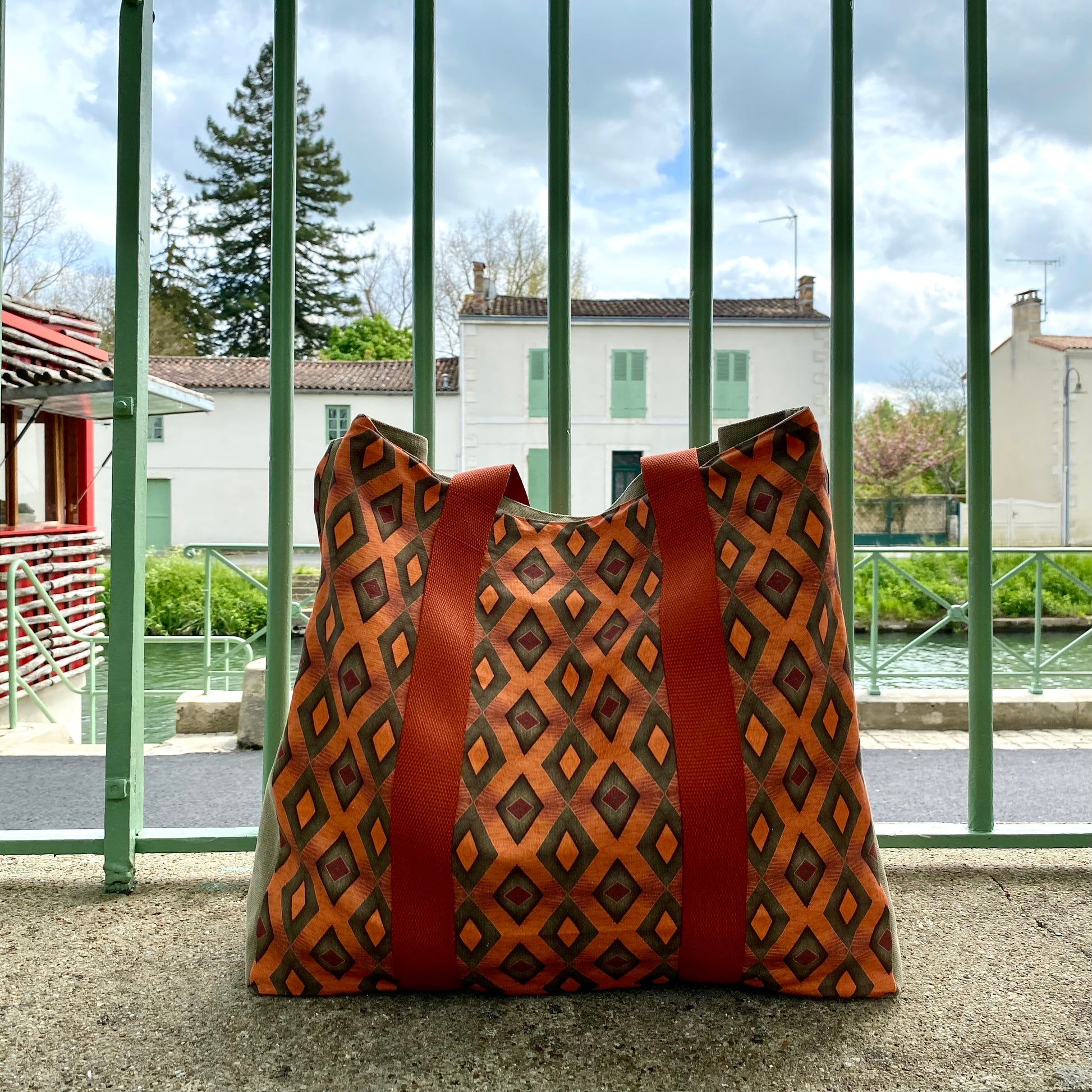[html] <img src= »grand-cabas-frehel-presente-debout-face-exterieure-vue-sur-motif-frehel-et-sangle-couleur-brique-arriere-grille-devant-paysage-basque» /> [/html]